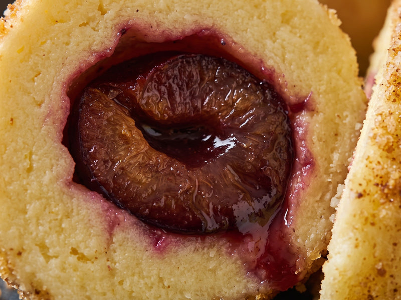 A close-up cross-section of a traditional Polish plum dumpling showing the soft potato dough enclosing a sweet, cinnamon-scented plum centre.