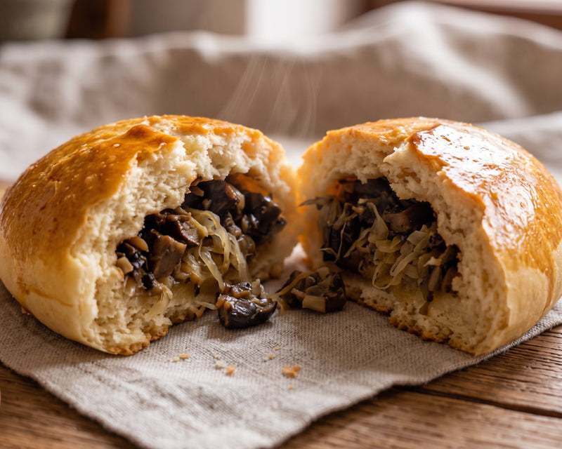 A close-up view of a freshly baked Polish hand pie torn in half, revealing a steaming hot filling of sauerkraut and mushrooms inside a soft, golden-brown yeast dough crust resting on a linen napkin.