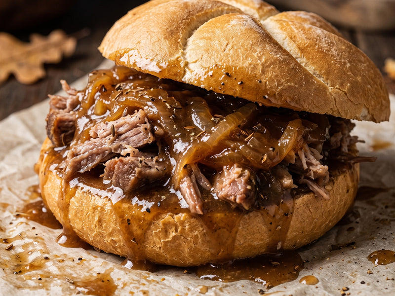 A close-up shot of a pulled pork sandwich on a rustic wooden table, filled with caramelized onions and rich onion sauce on a white paper bag.