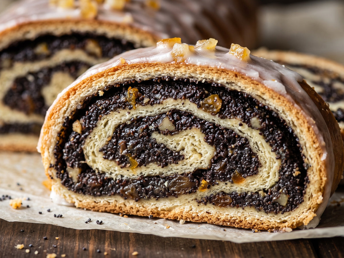 A close-up cross-section of a sliced Makowiec, revealing tight swirls of soft yeast dough and dark poppy seed filling studded with raisins, finished with a white icing glaze and candied orange peel.