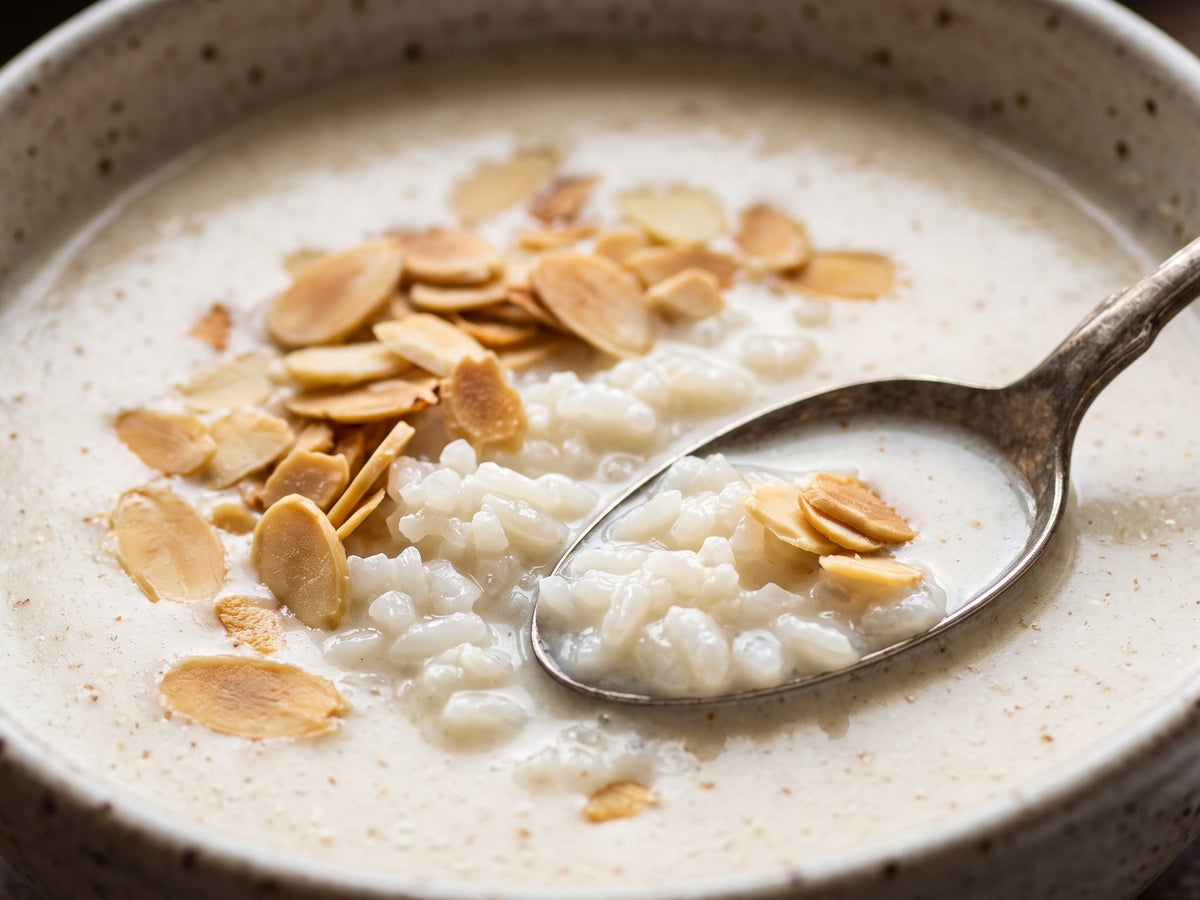 A close-up view of a ceramic bowl filled with silky Polish almond soup and plump white rice, topped with crunchy toasted almond flakes.